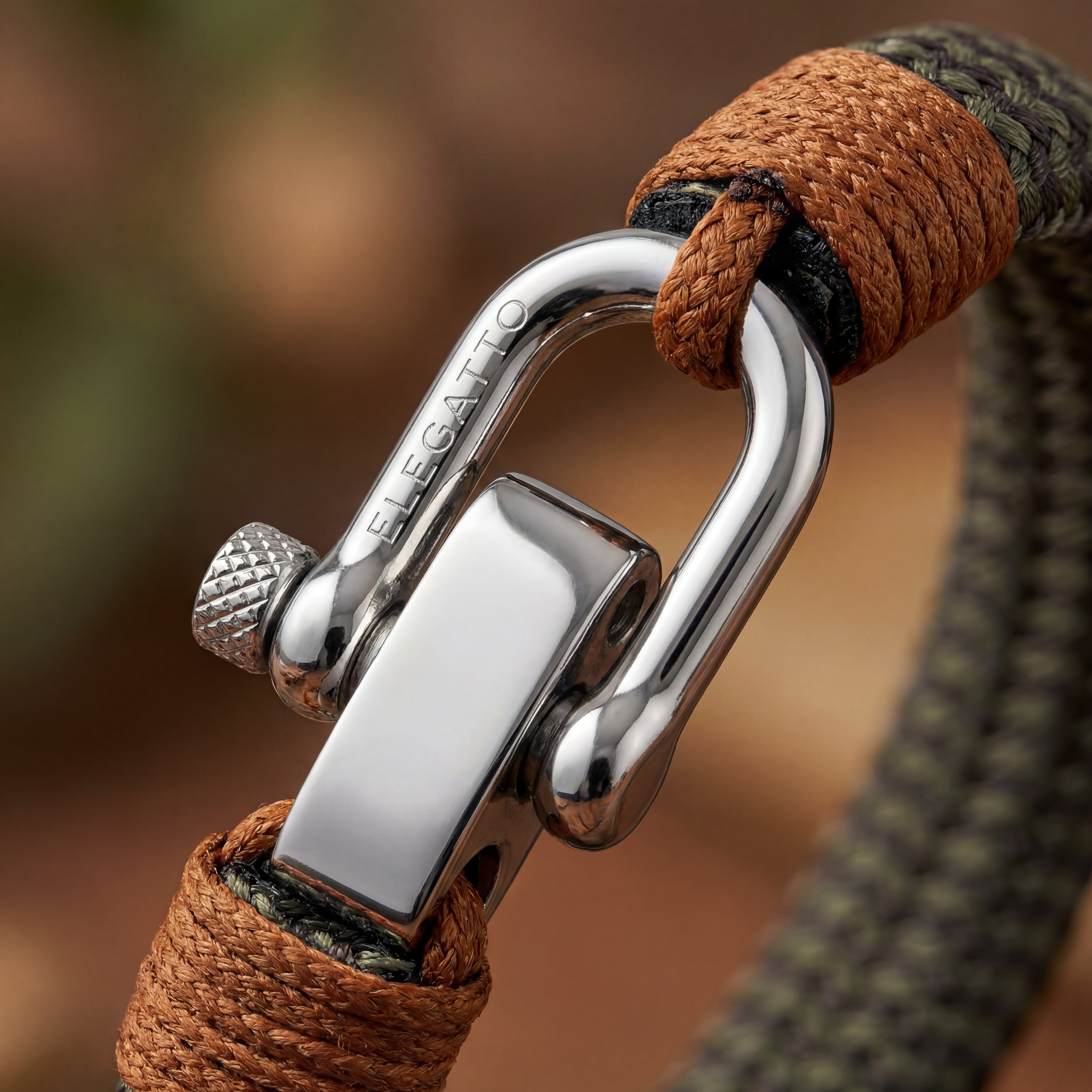 Close-up detail of the polished silver shackle clasp on the Altus bracelet. Showing the texture of the durable orange cord and brown bindings.