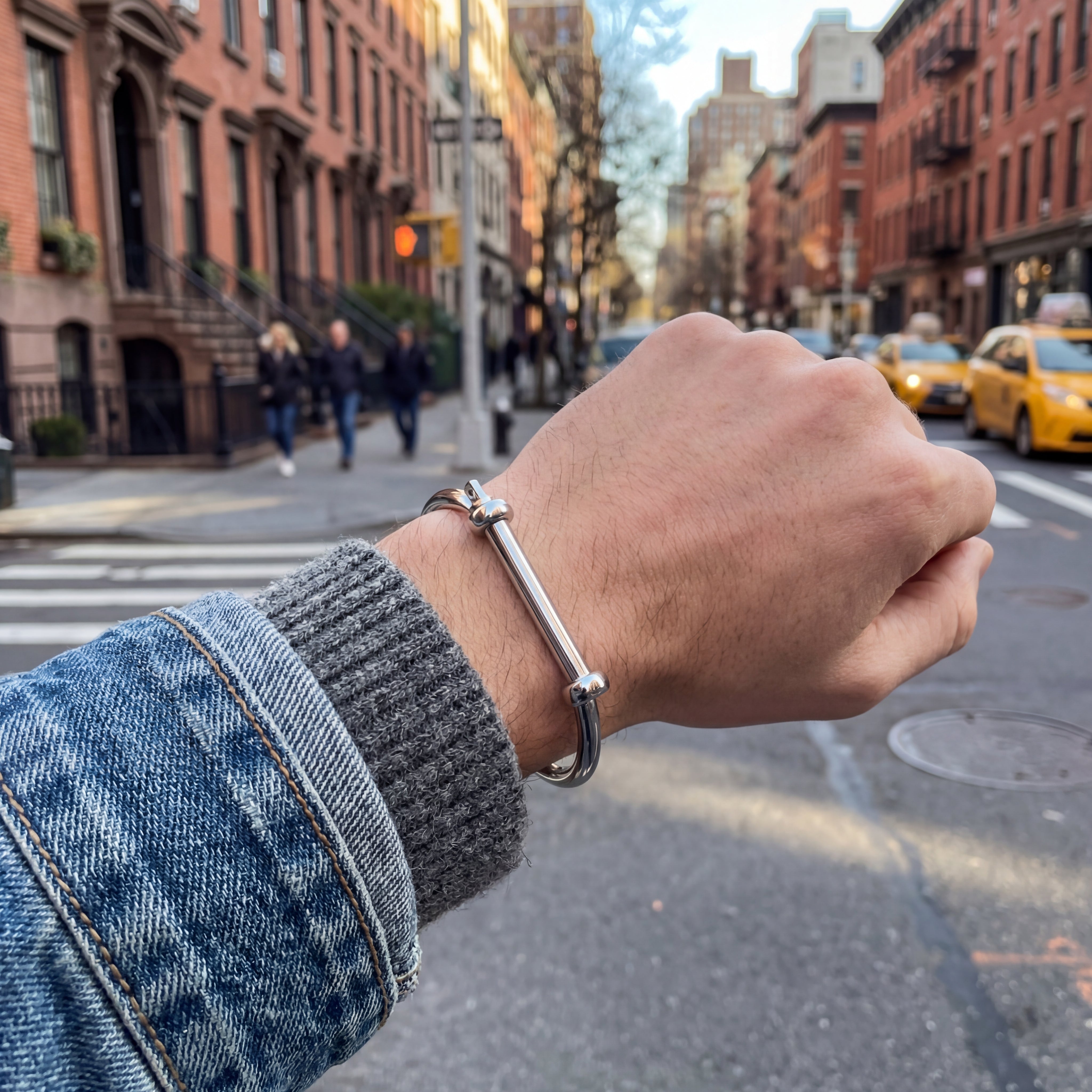 Hand wearing a silver bracelet with a city street in the background