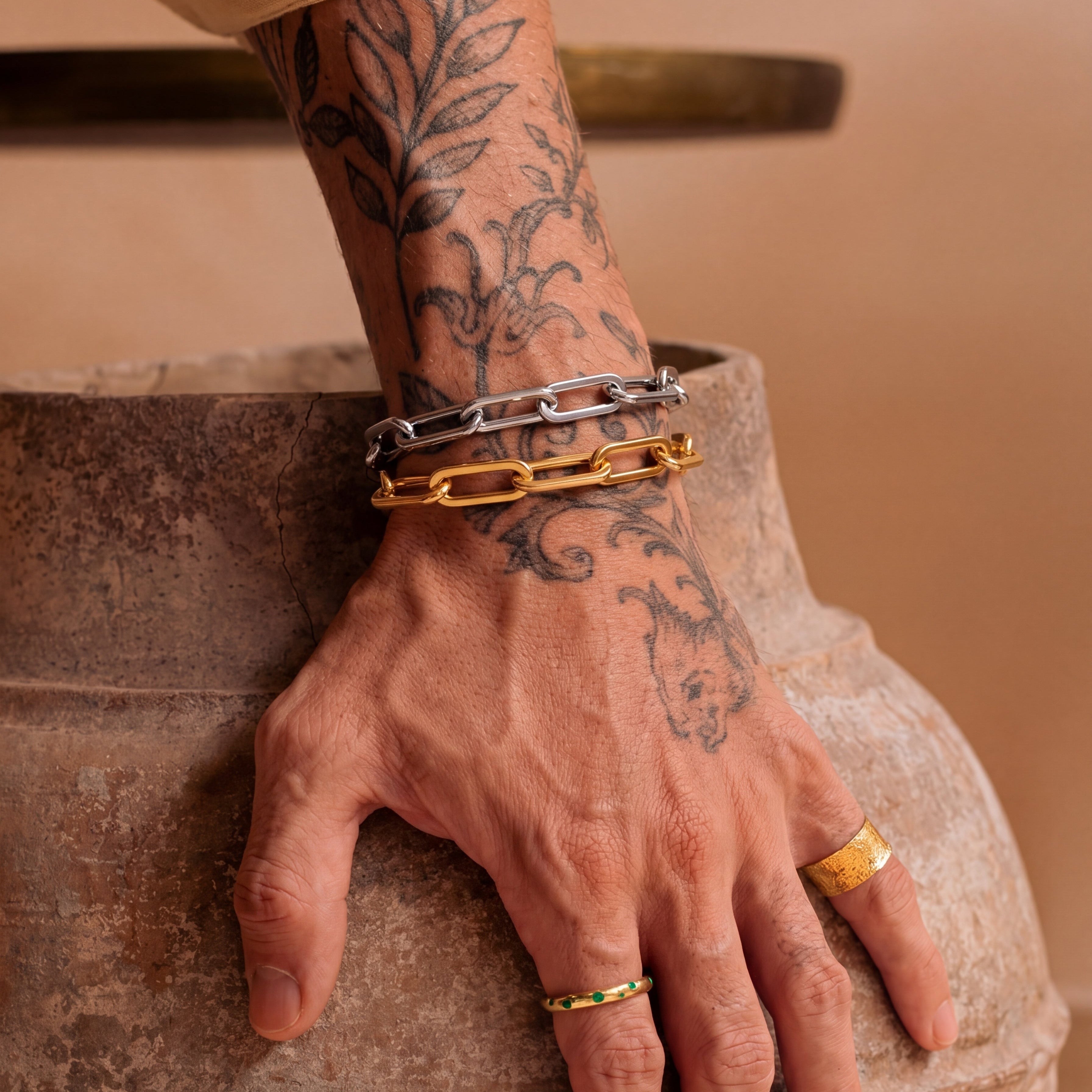 Hand with tattoos wearing gold bracelets and rings on a stone surface