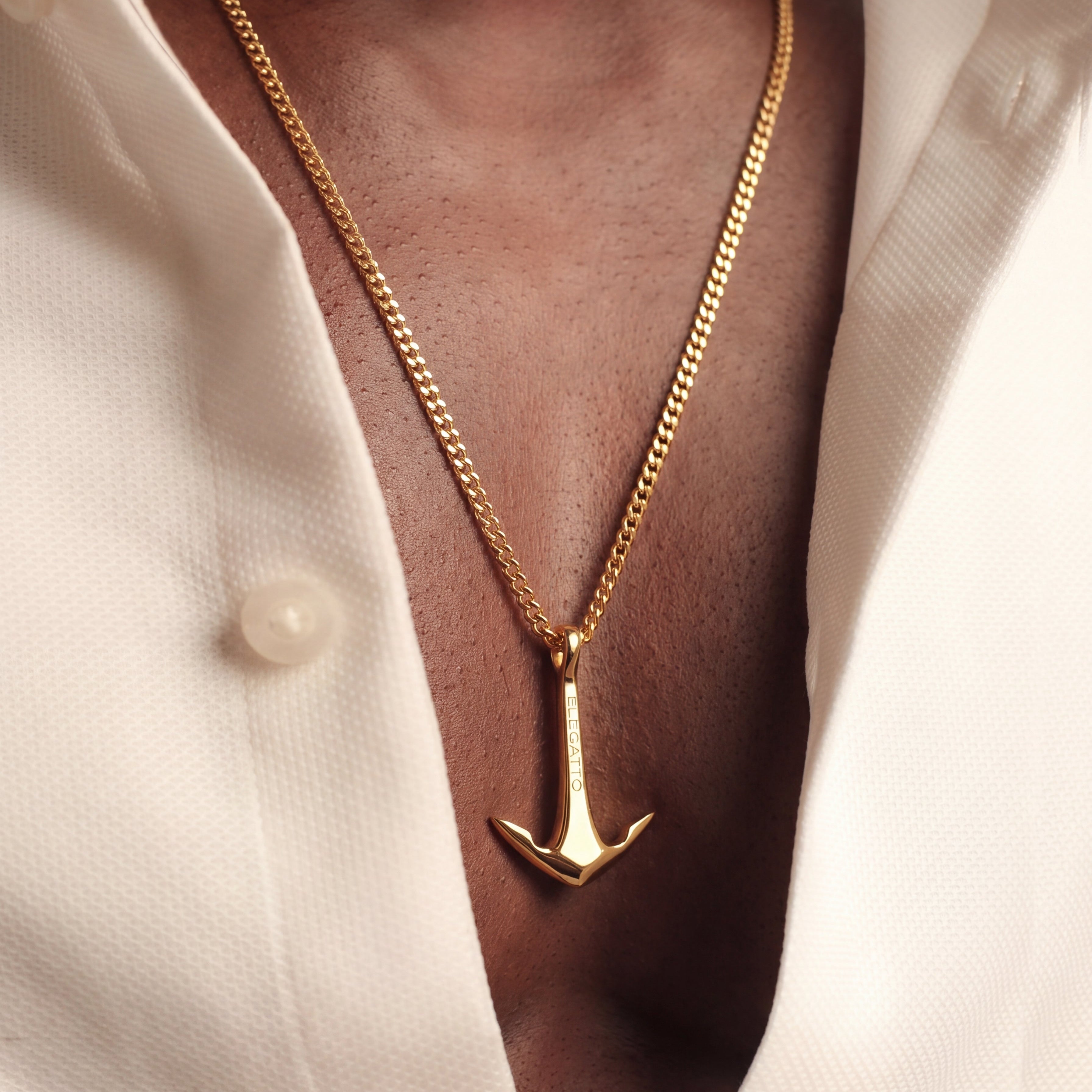 Gold anchor necklace worn by a person with a white shirt