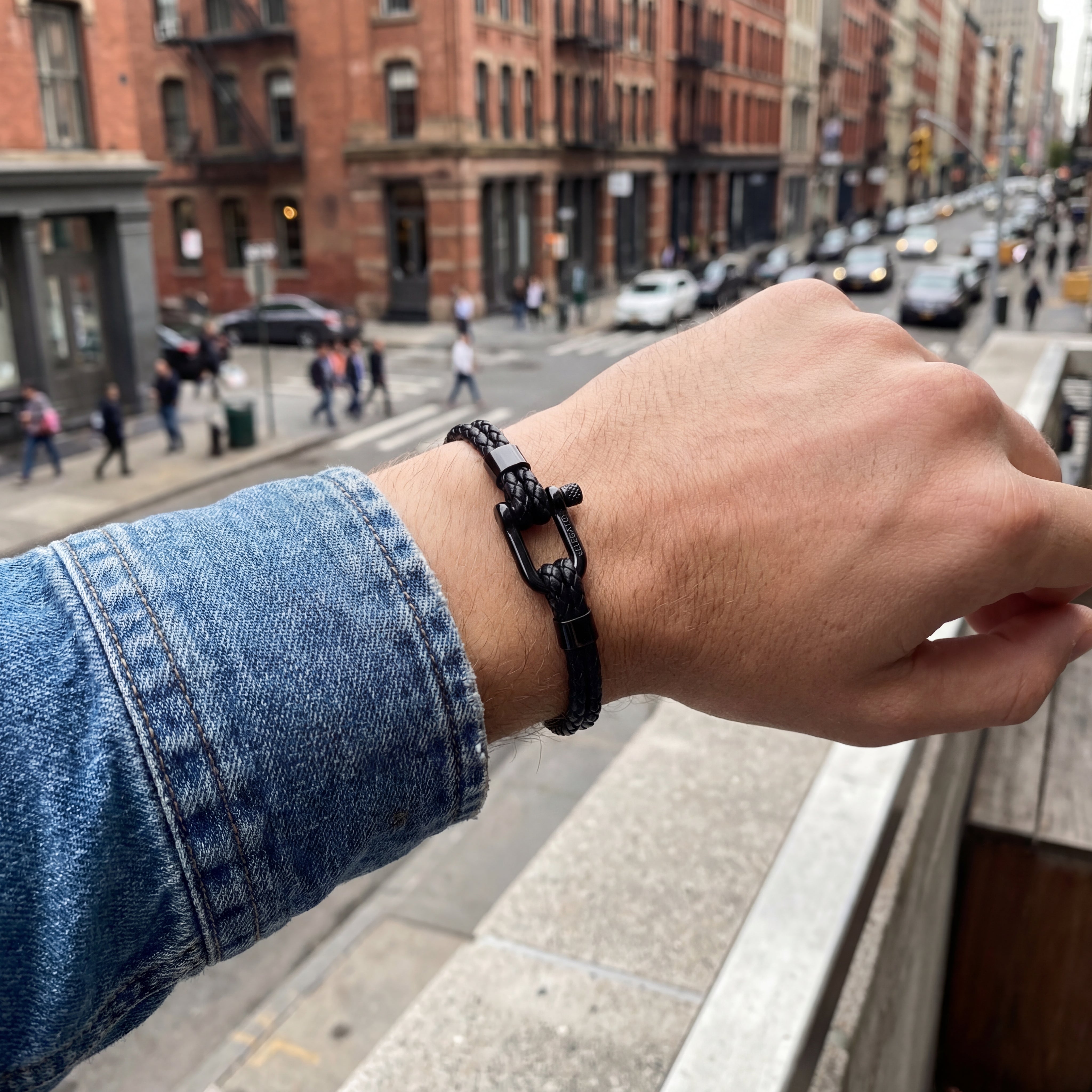 Hand wearing a black bracelet with a city street in the background